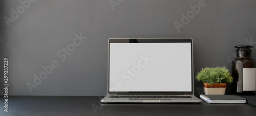 Open blank screen laptop computer in dark trendy workplace with copy space