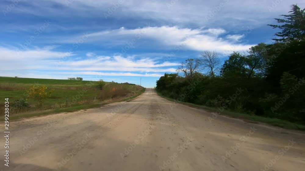 POV through driver's window while driving through rural Iowa; viewing farmstead, trees, ditches and fields