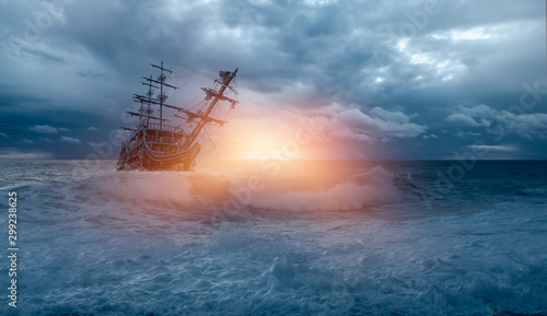 Sailing old ship in storm sea against heavy sunset clouds