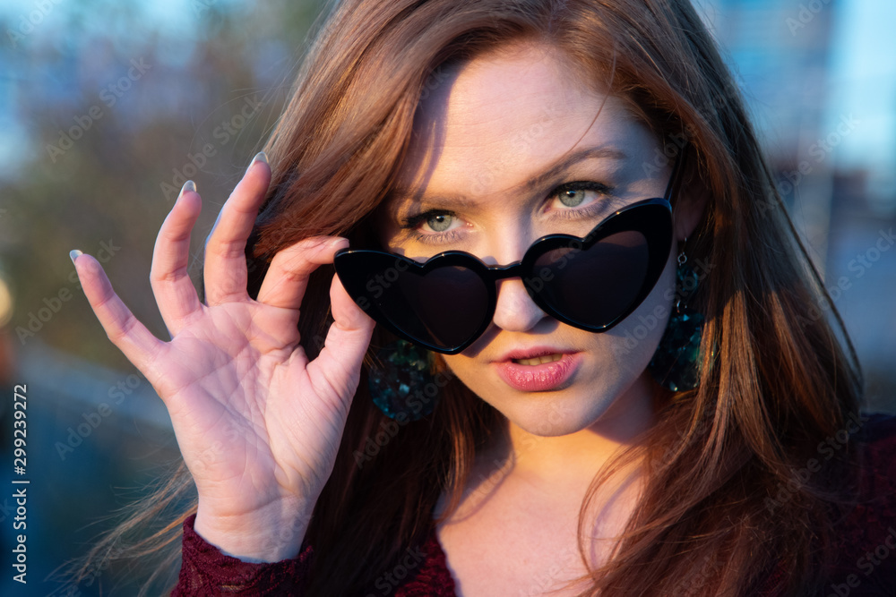 Red head young woman head and hand with heart shapped sunglasses eyes looking at camera Red head young woman head and hand with heart shapped sunglasses eyes looking at camera
