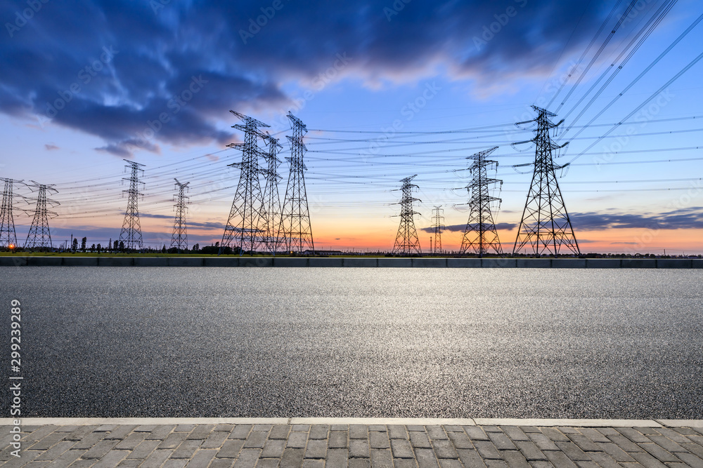 Empty asphalt road and high voltage electricity tower landscape at sunset.