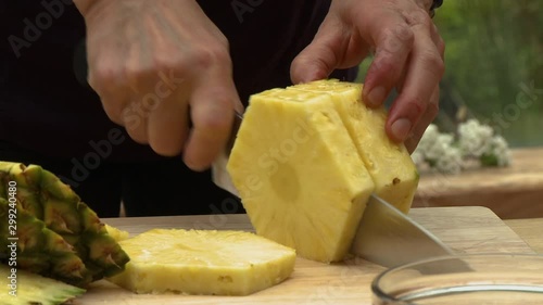 Steady, above angle, medium close up shot of a halved pineapple resting on a cutting board. Two wine glasses sit nearby.