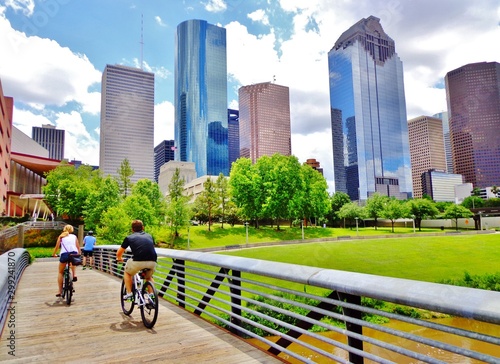 Bicyclists cross wooden bridge in Buffalo Bayou Park, with a beautiful view of downtown Houston (skyline / skyscrapers) in background on a summer day - Houston, Texas, USA  photo