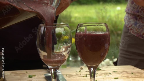 Handheld, medium close up shot of thick, red juice being poured into wine glasses.