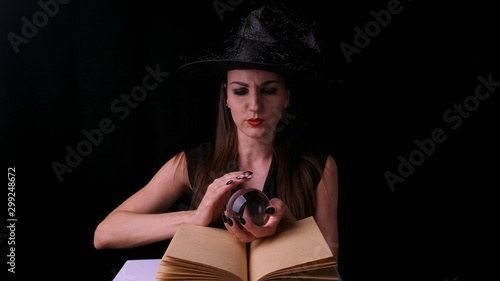 Attractive witch, on a black background, holds a candle over a spell book in her hands and screams. Front view