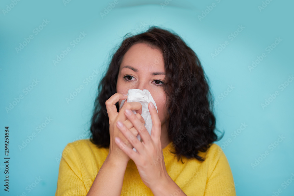 Burnette woman blowing nose into tissue. Flu cold or allergy symptom. Sick woman girl sneezing in tissue on blue. Health care. Burnette woman blowing nose into tissue. Flu cold or allergy symptom. Sick woman girl sneezing in tissue on blue. Health care.