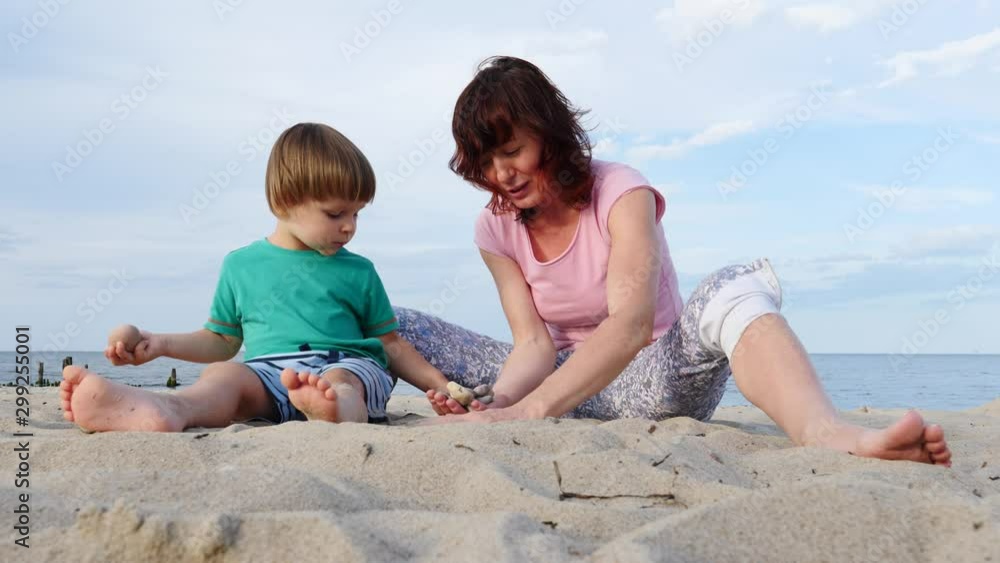 Mother playing with little child boy on sand beach. Adult woman and her son enjoying summer day on seshore. Family holiday at sea. Slow motion Mother playing with little child boy on sand beach. Adult woman and her son enjoying summer day on seshore. Family holiday at sea. Slow motion