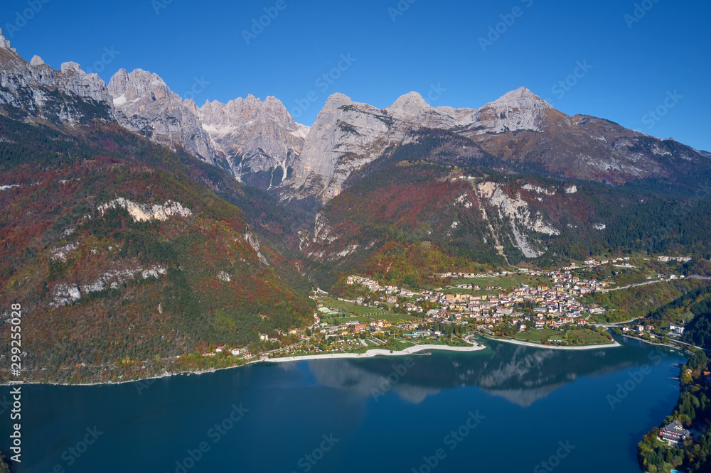 Aerial view of Lake Molveno, north of Italy in the background the city of Molveno, Alps, blue sky. Reflection of mountains in water. Autumn season. Multi-colored palette of colors