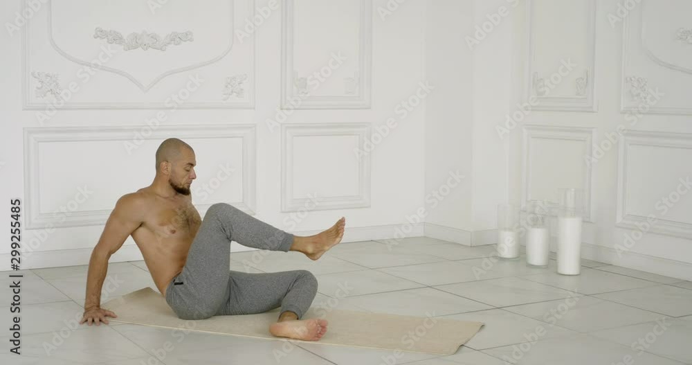muscular bald man with bare torso demonstrates rajakapotasana sitting on foam mat in light studio slow motion muscular bald man with bare torso demonstrates rajakapotasana sitting on foam mat in light studio slow motion
