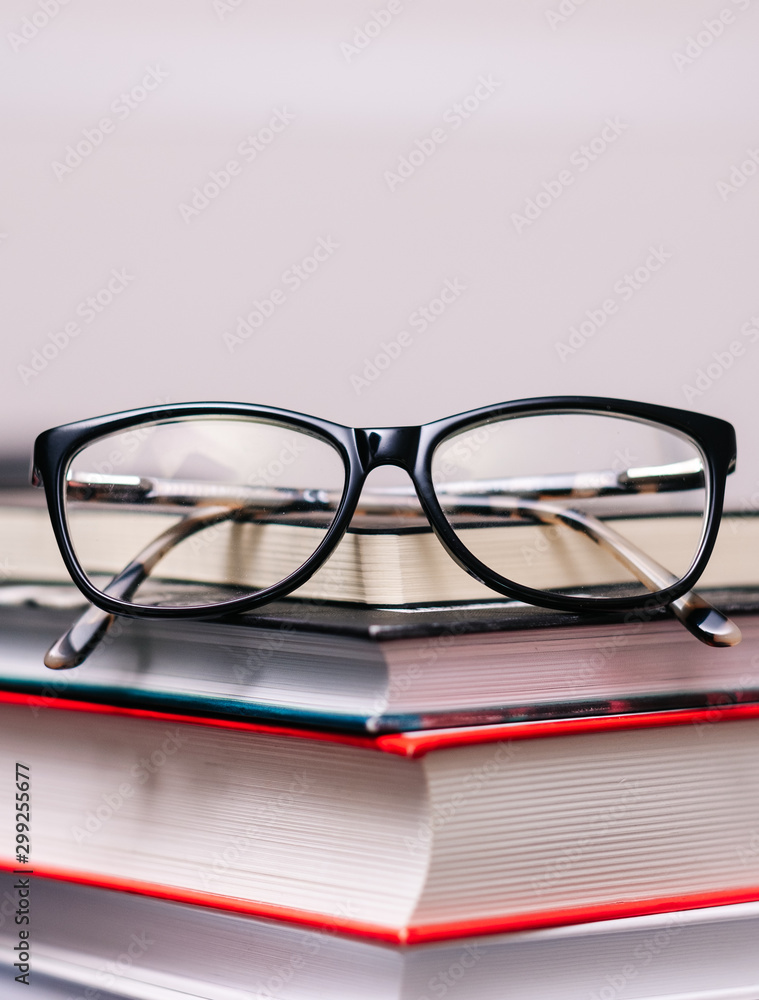 Pile of books and eyeglasses on it on wooden table, close up Pile of books and eyeglasses on it on wooden table, close up