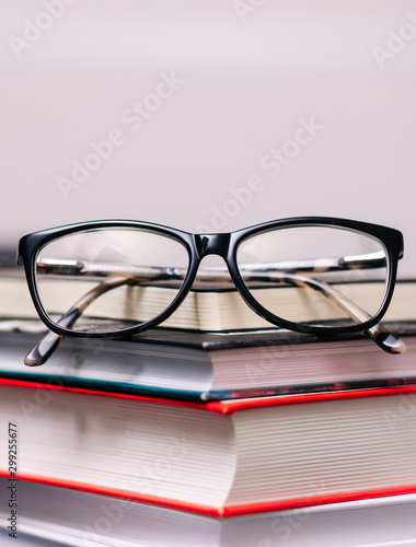 Pile of books and eyeglasses on it on wooden table, close up