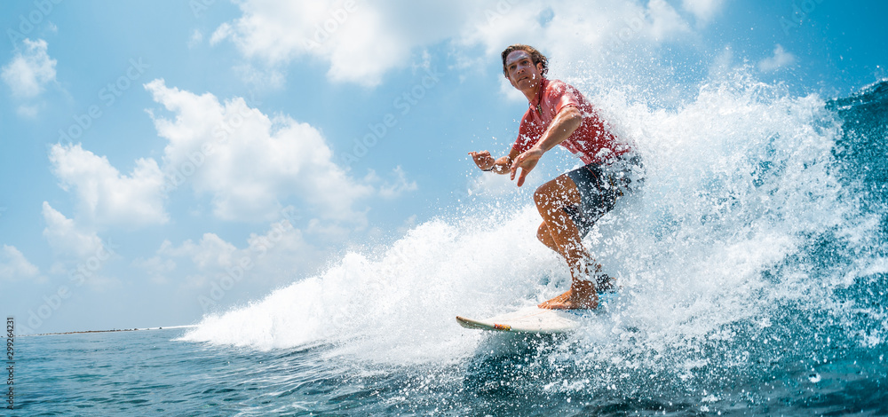Fototapeta Young caucasian man surfs the ocean wave and makes a lot of splashes into the camera. Chickens surf spot in Maldives