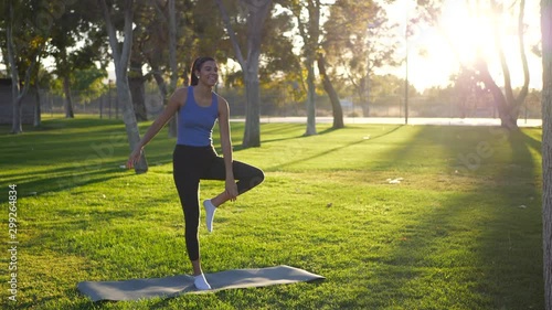A beautiful young woman yogi laughing while falling over and losing balance in a one legged prayer hands yoga pose at the park at sunrise. photo