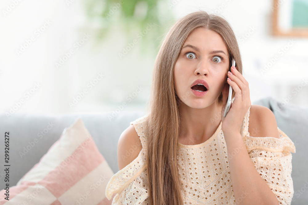 Surprised young woman talking by mobile phone at home Surprised young woman talking by mobile phone at home
