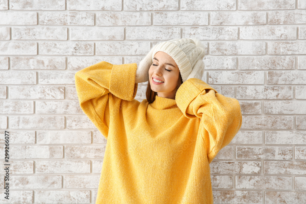 Beautiful young woman in warm winter clothes against brick wall