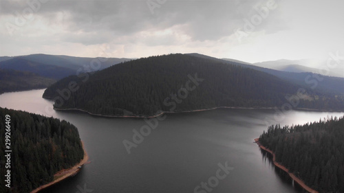 Aerial Footage of Large Lake and mountains surrounded by Pine Forest trees, Romania