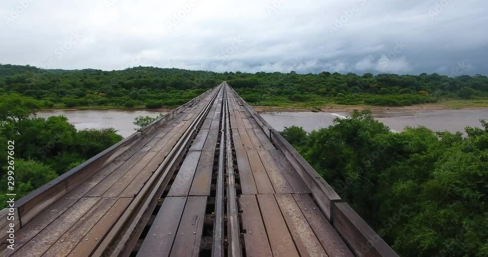 A Dirt Road Connected by a Hanging Bridge that Passes Over a Brown River A Dirt Road Connected by a Hanging Bridge that Passes Over a Brown River