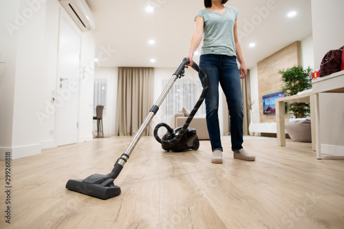 Wide angle photo of woman housewife or maid or service worker hoovering with vacuum cleaner in bright luxury appartment.