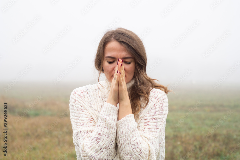 Girl closed her eyes, praying in a field during beautiful fog. Hands folded in prayer concept for faith Girl closed her eyes, praying in a field during beautiful fog. Hands folded in prayer concept for faith