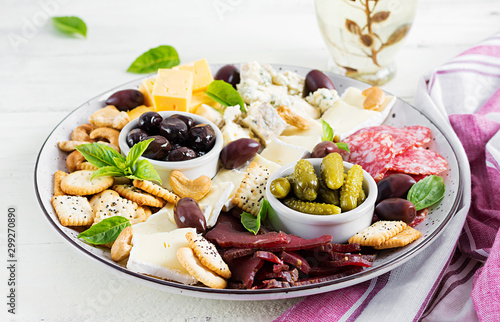 Antipasto platter with basturma, salami, blue cheese, nuts, pickles and olives on a white wooden background.