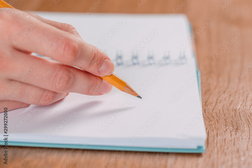 Close up of woman's hands writing in spiral notepad placed on wooden desktop with various items Close up of woman's hands writing in spiral notepad placed on wooden desktop with various items