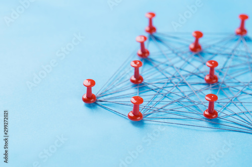 network with red pins and string, An arrangement of colorful pins linked together with string on a blue background suggesting a network of connections.