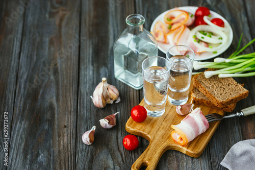 Vodka with lard and green onion on wooden background. Alcohol pure craft drink and traditional snacks, tomatos and bread toast. Negative space. Celebrating food and delicious.