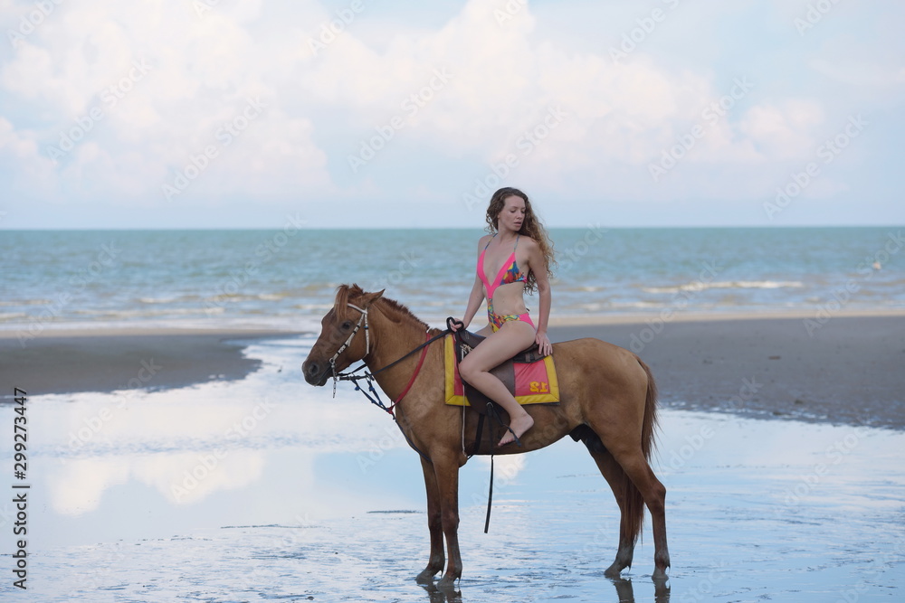 A pretty woman in a bikini is happily riding a horse on the beach. A pretty woman in a bikini is happily riding a horse on the beach.