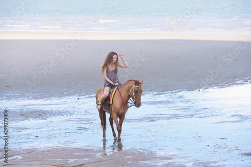 A pretty woman in a bikini is happily riding a horse on the beach.