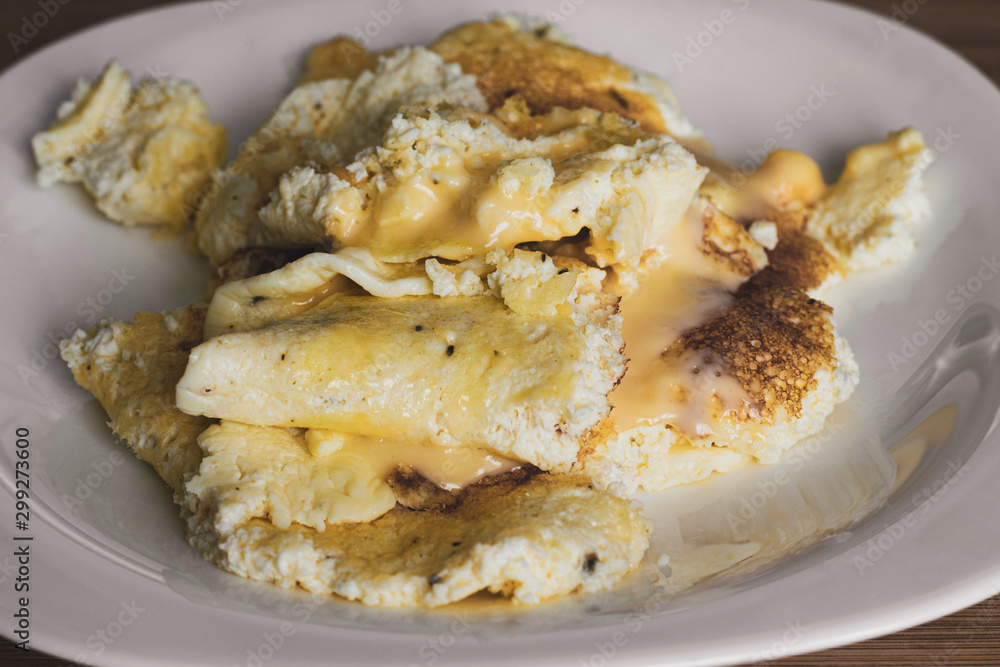 Tasty yellow chicken omelet with melted cheese on a white plate. Close-up