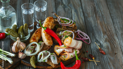 Vodka with lard, salted fish and vegetables, sausages on wooden background. Alcohol pure craft drink and traditional snack, tomatos, onion, cucumbers. Negative space. Celebrating food and delicious.