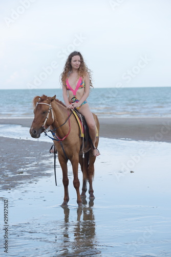 Beautiful girl in a swimsuit is happily riding a horse on the sand.