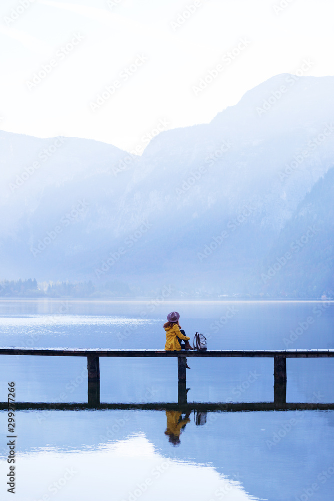 Naklejka premium tourist girl in a hat and with a backpack sitting on a wooden bridge