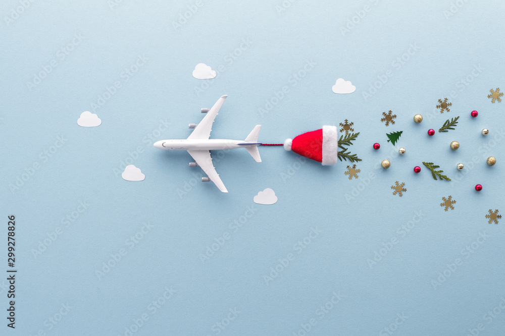 Fototapeta Christmas composition. Airplane flying in sky clouds fir star santa hat top view background with copy space for your text. Flat lay.