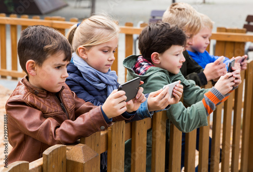 Kids playing with smartphones near wooden fence
