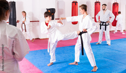 Kids in kimonos exercising techniques in pair during taekwondo class at gym