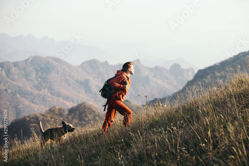 Fototapeta Beautiful woman traveler climbs uphill with a dog on a background of mountain views