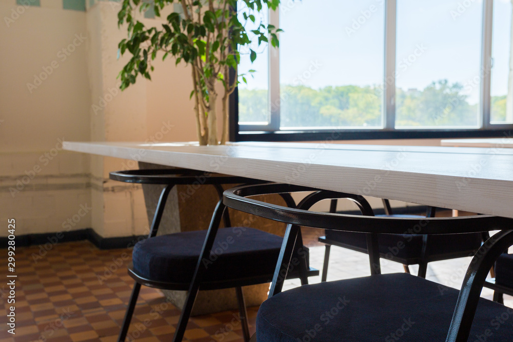 Fototapeta premium Loft style office with white brick walls and concrete columns. There is a meeting area with a large white table with black chairs