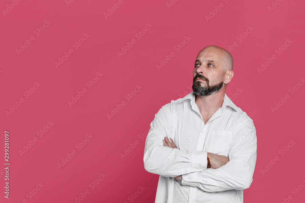Serious middle-aged man with folded arms and a deadpan expression posing in front of a pink background with copy space Serious middle-aged man with folded arms and a deadpan expression posing in front of a pink background with copy space