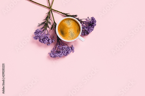 Cup of coffee with flowers on pink background.