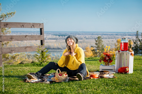 Young adult beautiful woman in nature on picnic with plaid, pumpkins and autumn scenery