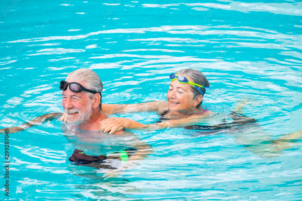 two seniors or mature caucasia people together at the swimming pool - active woman and man doing exercise together at the pool to be healthy - summer time in vacations