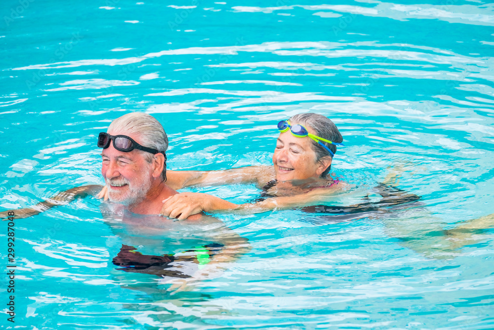 Fototapeta premium two seniors or mature caucasia people together at the swimming pool - active woman and man doing exercise together at the pool to be healthy - summer time in vacations