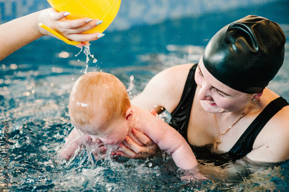 Young mother, happy little girl in the pool. Teaches infant child to swim. Enjoy the first day of swimming in water. Mom holds child. doing exercises. hand pours a mug of water on the baby's head