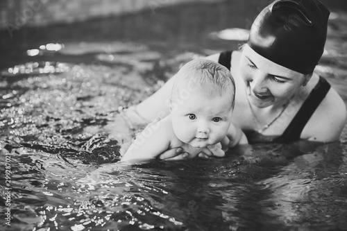 Young mother, happy little girl in pool. Teaches infant child to swim. Enjoy first day of swimming in water. Mom hold child preparing for diving exercises. hand leading child on water. black and white