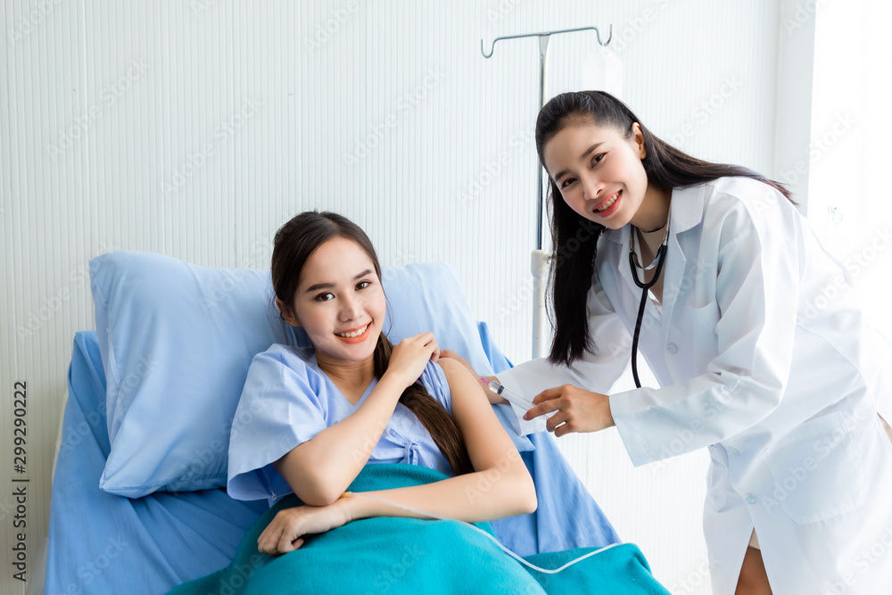 Obraz premium Asian young female doctor with syringe to the arm of Asian young female patient on Bed for better healing In the room hospital background.