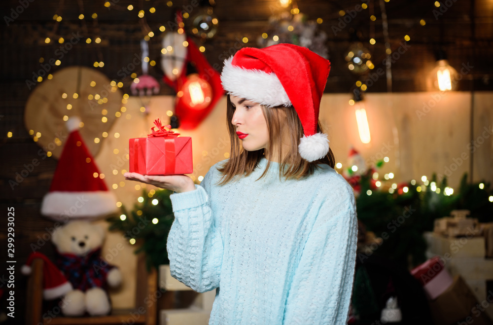 Cozy christmas atmosphere. Believe in miracle. Woman santa claus hat on christmas eve. Lady adorable face celebrate christmas at home. Open her gift. Girl stylish makeup red lips hold christmas gift