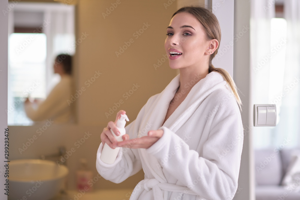 Young woman with flawless skin, applying moisturizing cream on her face. Photo of woman after bath in white bathrobe and towel on white background. Skin care concept Young woman with flawless skin, applying moisturizing cream on her face. Photo of woman after bath in white bathrobe and towel on white background. Skin care concept