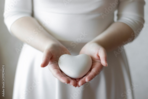 Women's hands are holding a small white plaster heart.