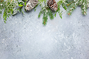 Christmas or winter background with a border of green and frosted evergreen branches and pine cones on a grey vintage board. Flat lay